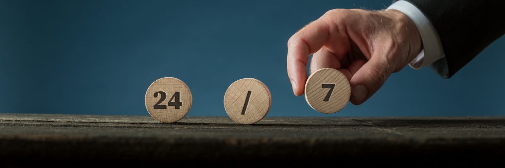 Wide view image of a hand of a businessman assembling a 24/7 sign with wooden cut circles. Over blue background.