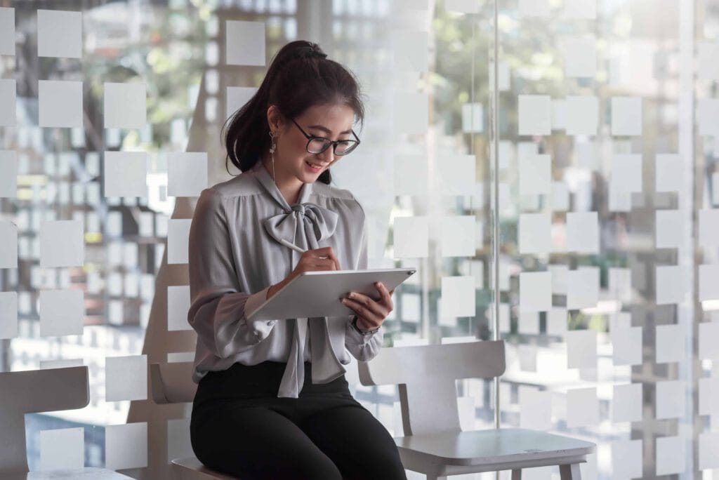 Beautiful smart Asian business woman taking notes on the tablet in his chair sitting at the office. Asia woman waiting for job interview.